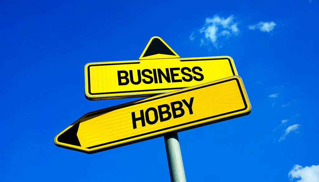Yellow street sign with a panel that reads "Hobby" pointing left and a panel that reads "Business" pointing up.